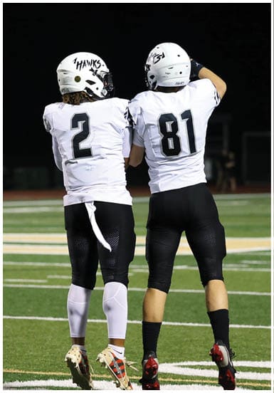 Two people wearing white football helmets and jerseys with the number 81 on one are standing on a football field at night. Descripci n generada con IA