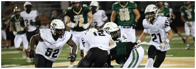 People wearing football uniforms are actively engaged in a game on a field with one player attempting to tackle another. Descripci n generada con IA