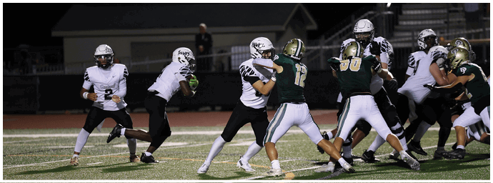 People wearing football uniforms are engaged in a play on a lit field during a nighttime game. Descripci n generada con IA