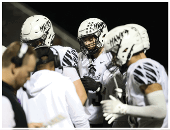 A person wearing a white football uniform and helmet is looking downward with a focused expression. Descripci n generada con IA