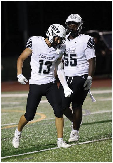 A person wearing a white football helmet and jersey with the number 13 is celebrating on a football field with another person in a similar uniform standing nearby. Descripci n generada con IA