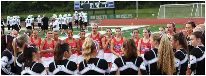 A group of people in sports uniforms are gathered on a field near a scoreboard displaying a tied score during a daytime outdoor event. Descripci n generada con IA