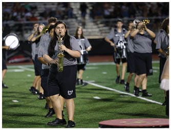 People wearing matching gray shirts are playing brass and woodwind instruments in a band setting. Descripci n generada con IA