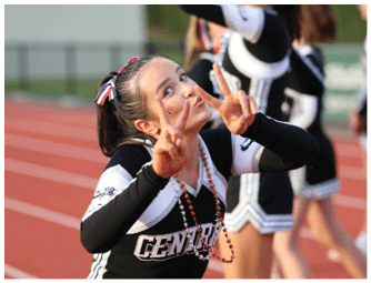 A person in a cheerleading uniform with “CENTRAL" on the front is making peace signs with both hands and smiling on a sports field. Descripci n generada con IA