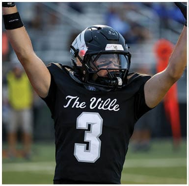 A person wearing a black football helmet and jersey is raising one arm, appearing focused during a game. Descripci n generada con IA