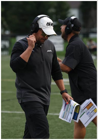 Two adults wearing headsets and casual sportswear appear to be engaged in a focused conversation outdoors. Descripci n generada con IA