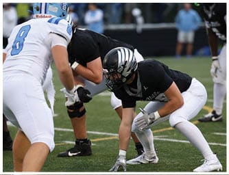 People in football uniforms are positioned on a field preparing for a play during a game. Descripci n generada con IA