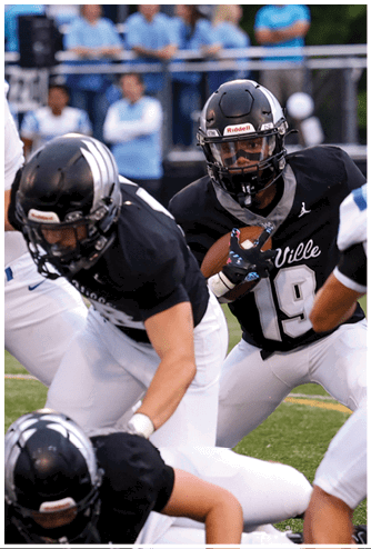 A person wearing a black football uniform with the number 19 is holding a football and appears to be running or preparing to make a play during a game. Descripci n generada con IA
