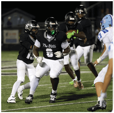 People wearing black and white football uniforms are actively playing on a grassy field during a nighttime game. Descripci n generada con IA