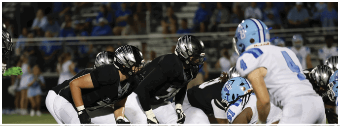 People in football uniforms are positioned on a field, preparing for a play during a game. Descripci n generada con IA