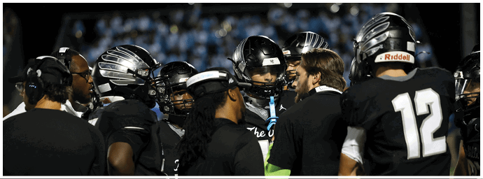 Several people wearing black sports jerseys and white pants are standing closely together, likely during a team huddle or discussion. Descripci n generada con IA