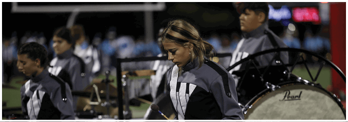 People in matching uniforms are playing percussion instruments in a band setting. Descripci n generada con IA