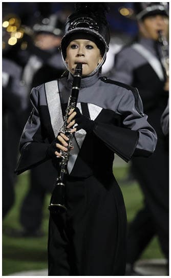 A person in a marching band uniform is playing a clarinet during a performance on a field. Descripci n generada con IA
