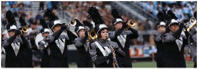 People in matching band uniforms are playing brass and woodwind instruments while marching on a field. Descripci n generada con IA