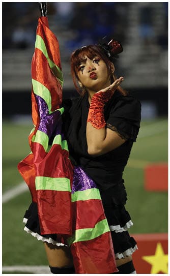 A person wearing a black outfit with a colorful skirt and red lace gloves is blowing a kiss. Descripci n generada con IA