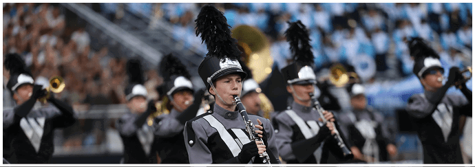 A group of people in marching band uniforms with tall black plumes are playing clarinets and brass instruments during a performance. Descripci n generada con IA