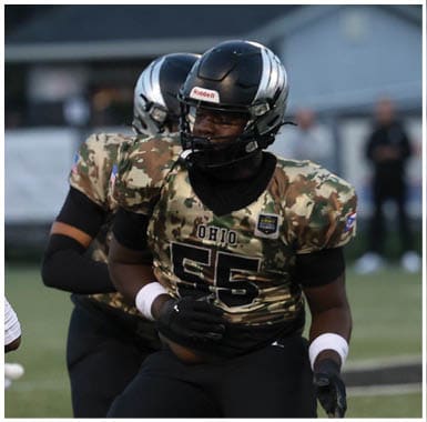 Two people wearing camouflage football uniforms and helmets are on a field, with one person in the foreground and the other slightly behind. Descripci n generada con IA