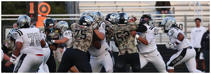 A group of people in football uniforms are engaged in a play on a football field with one person holding the ball and others blocking or running. Descripci n generada con IA
