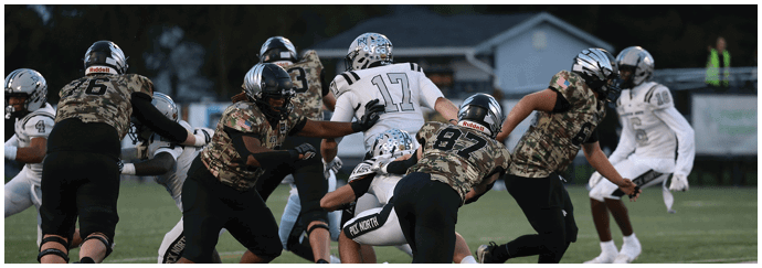 Several people wearing football uniforms are engaged in a play on a grassy field during a game. Descripci n generada con IA
