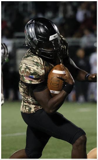 Two people in football uniforms are actively engaged in a play on a grassy field with one holding the ball and the other running nearby. Descripci n generada con IA