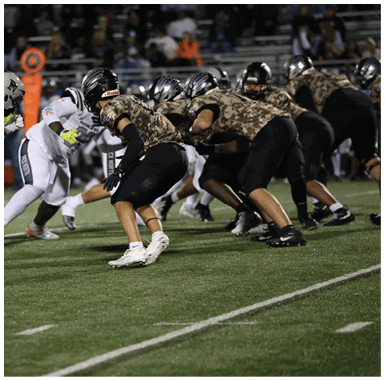 Several people in football uniforms are actively engaged in a play on a grassy field during a game. Descripci n generada con IA