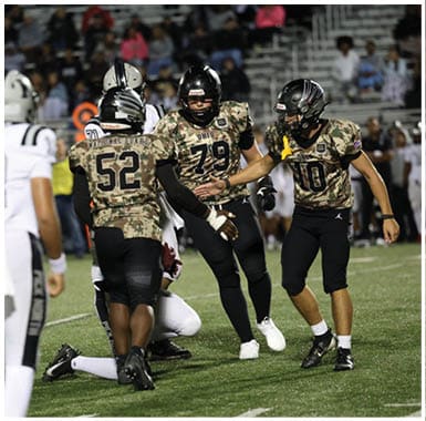 People wearing black and white football uniforms are actively playing on a grassy field during a nighttime game. Descripci n generada con IA