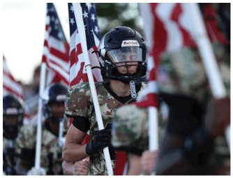 People wearing camouflage uniforms and helmets are holding American flags in a formation. Descripci n generada con IA