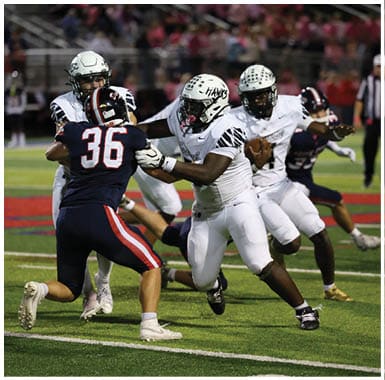 Two people in white football uniforms are engaged in a play on a football field, with one person holding the ball and the other preparing to block or catch. Descripci n generada con IA
