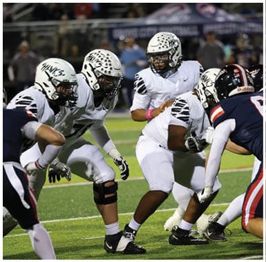 People in football uniforms from two teams are positioned on a field preparing for a play during a game. Descripci n generada con IA