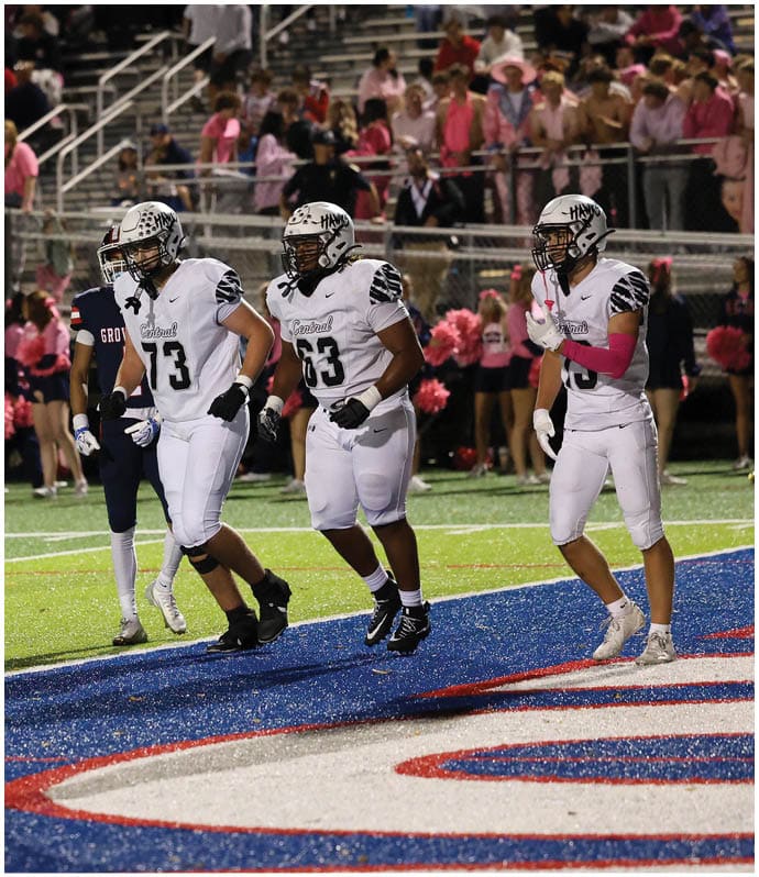 Players in football uniforms are on a field near the end zone with spectators in the stands behind them. Descripci n generada con IA