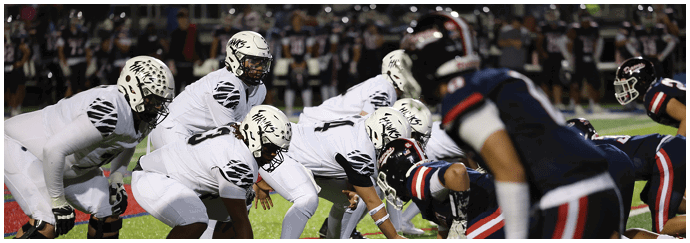 Two opposing American football teams are lined up facing each other on a field, ready for the next play. Descripci n generada con IA