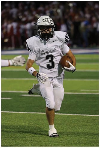 A person wearing a white football uniform with the number 3 is running on a green field while holding a football. Descripci n generada con IA