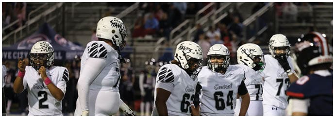 A group of people wearing white football uniforms and helmets are standing together on a field during a game. Descripci n generada con IA
