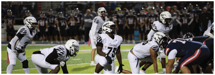 People in football uniforms are lined up on a field preparing for a play during a game. Descripci n generada con IA