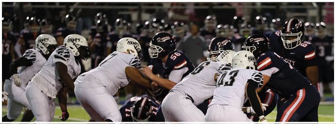 People in football uniforms are engaged in a play on a field with a red end zone and a crowd in the background. Descripci n generada con IA