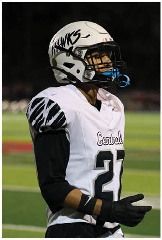 A person wearing a white football uniform with the number 27 and a helmet is standing on a football field at night. Descripci n generada con IA