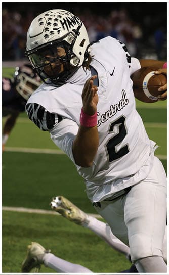 A person wearing a white sports jersey with the number 2 is holding a football close to their head on a green field. Descripci n generada con IA