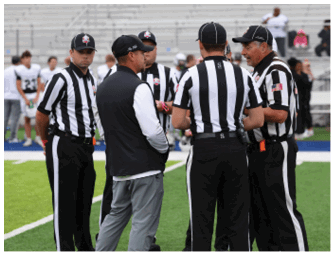 Several people wearing black and white striped referee uniforms are standing on a sports field engaged in conversation. Descripci n generada con IA