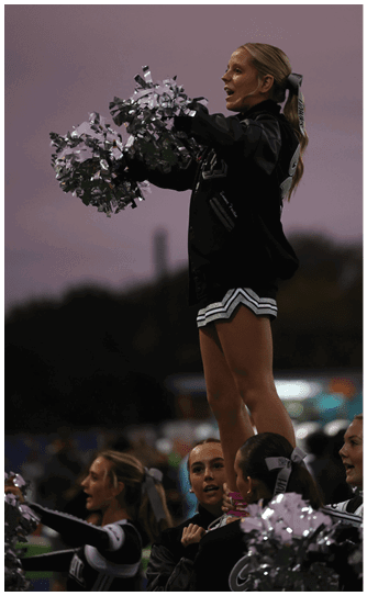 A person wearing a dark jacket is enthusiastically holding and shaking silver pom-poms against a plain background. Descripci n generada con IA