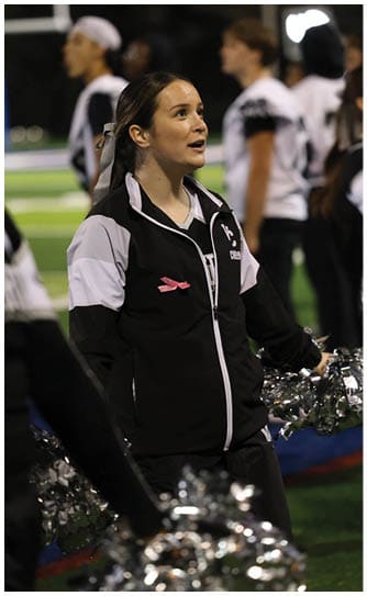 A person with long hair tied back is wearing a sports jacket and looking upwards with an engaged expression in an outdoor setting. Descripci n generada con IA