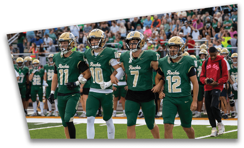 People wearing black American Canyon football uniforms and helmets are standing on a football field at night. Description generated by AI