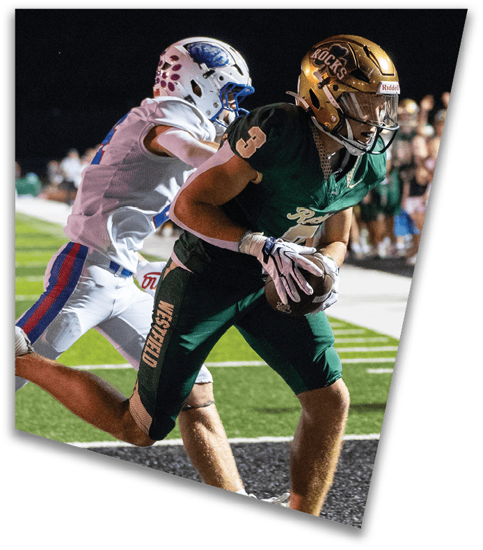A person wearing a dark football uniform and helmet with “American Canyon" on the jersey is kneeling on one knee on a field at night. Description generated by AI
