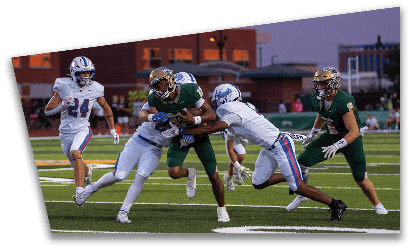 People wearing black American Canyon football uniforms and helmets are standing on a football field at night. Description generated by AI