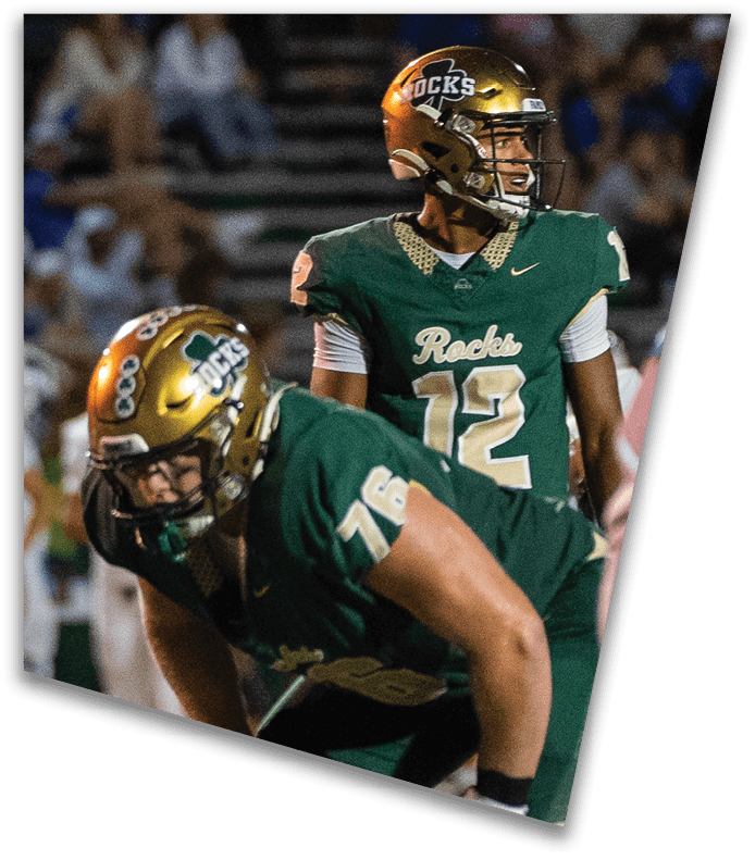 A person wearing a dark football uniform and helmet with “American Canyon" on the jersey is kneeling on one knee on a field at night. Description generated by AI