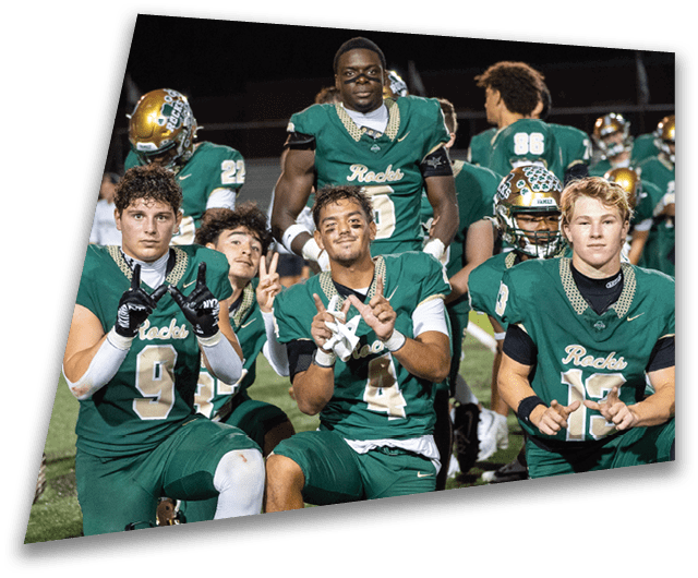 Four people in dark football uniforms and helmets stand in a row on a field, appearing focused and ready for action. Description generated by AI