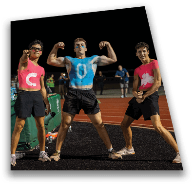 A person in football gear and helmet is crouched on a field with other players lined up in the background during a game. Description generated by AI