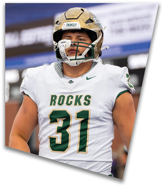 A person wearing a dark football uniform and helmet with “American Canyon" on the jersey is kneeling on one knee on a field at night. Description generated by AI