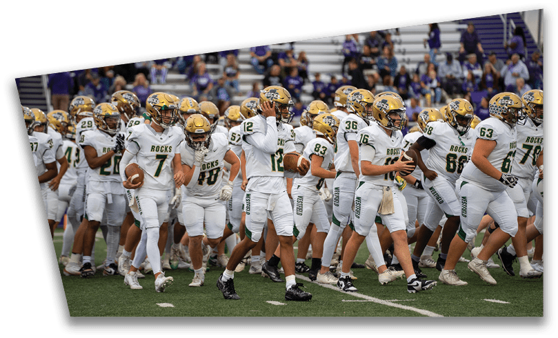 People wearing black American Canyon football uniforms and helmets are standing on a football field at night. Description generated by AI