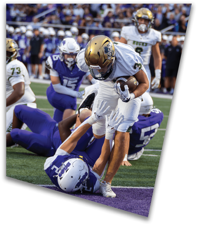 A person wearing a dark football uniform and helmet with “American Canyon" on the jersey is kneeling on one knee on a field at night. Description generated by AI
