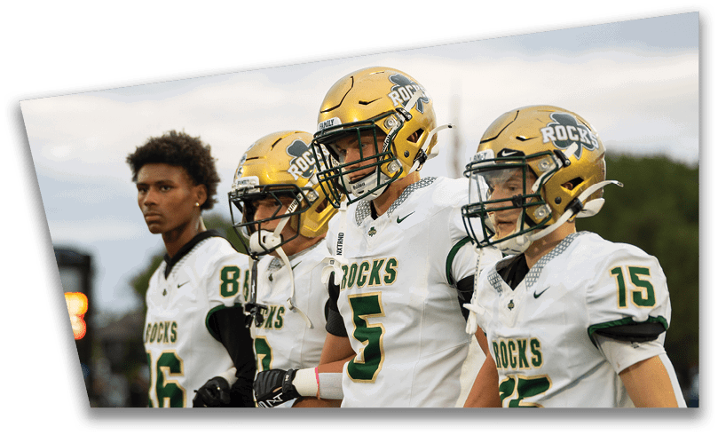 People wearing black American Canyon football uniforms and helmets are standing on a football field at night. Description generated by AI